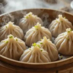 A plate of steaming vegan soup dumplings with a dipping sauce on the side.